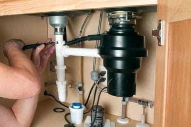 Plumber repairing a garbage disposal beneath a kitchen sink in Commerce City