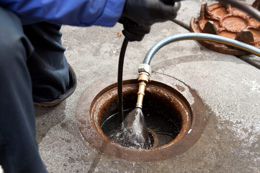 Plumber hydro jetting a sewer line through a manhole in Commerce City
